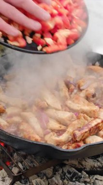 Genç adamın dikey görüntüleri sebzeleri tavada etle kızartıyor. Yemek, diyet, düşük kalori. Biber dilimleri tavaya soğanla düşer. Şenlik ateşinde sebze sote