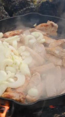 Bilinmeyen bir gencin kış vakti ateşte et ve soğan kızartırken çekilmiş dikey videosu. Yemek pişirme konsepti