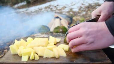 Bahar başında kamp ateşi ve ormanın yakınındaki tahta tahtada erkek ellerinin taze patates bıçağını kesmesi. Yemek pişirme konsepti