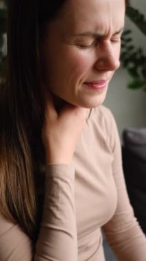 Evdeki kanepede oturan kadının acıdan çektiği dikey görüntüler. Sağlık ve tıbbi konsept. Boğazı ağrıyan, gripten dolayı bademcikleri iltihaplanan, sağlıksız, üzgün, beyaz bir kadın.