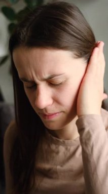 Üzgün genç bir kadının acı dolu kulağını tutarken aniden güçlü bir ağrı hissettiği dikey görüntüler. Sağlıksız beyaz kadın evdeki kanepede oturan acı veren otit iltihabından muzdarip. Sağlık sorunları kavramı