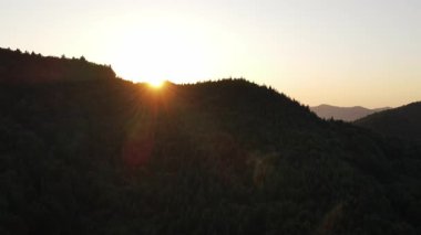 İnanılmaz dağların ve ılık günbatımının ya da yaz mevsiminde güneşin doğuşunun havadan görüntüsü. Dağ sırasının yeşil orman yamaçları silueti. Gökyüzündeki parlak güneş diski yavaşça dağların tepesine çıkar.