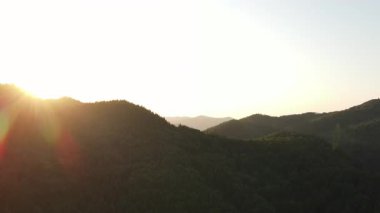 Sıcak günbatımında inanılmaz dağların insansız hava aracı görüntüsü. Dağ sırasının orman yamaçları. Güneşin parlak diski yavaşça dağların tepesine çıkar. Dramatik gün doğumu gökyüzü arkaplanı