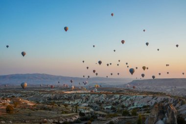 Kapadokya, Türkiye 'deki sıcak hava balonları filosunun güneş doğarken görüntüsü. Kapadokya popüler bir turizm merkezidir..