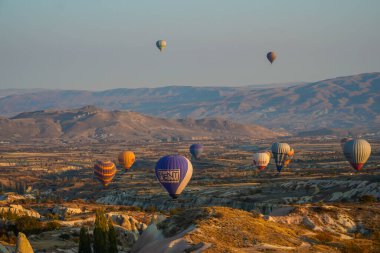 Kapadokya, Türkiye 'deki sıcak hava balonları filosunun güneş doğarken görüntüsü. Kapadokya popüler bir turizm merkezidir..