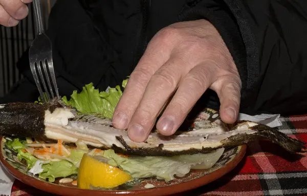 The process of eating fish in a restaurant. Butchering trout with a fork and hands. Close-up action.