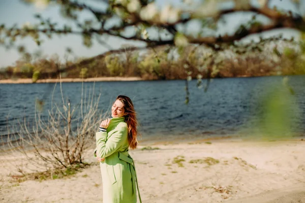 stylish woman in a green coat on the background of spring flowering and the rive
