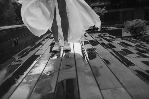 花嫁の白いドレスとスニーカーはライの後に水たまりを歩く — ストック写真