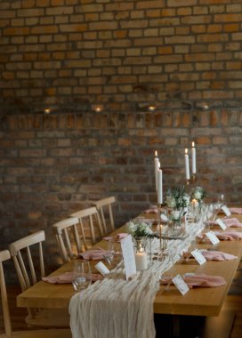 Kırsal tarzda bir şenlik masası. Mumlar ve çiçeklerle süslenmiş beyaz kumaşlar.