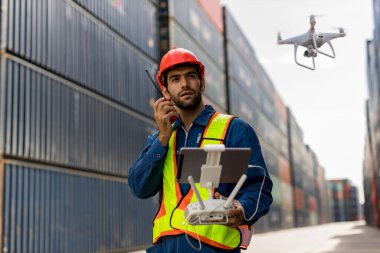 Ustabaşı ya da işçi konteynır limanında uzaktan kumandalı pilotsuz uçak kullanıyor. Foreman, nakliye limanında konteynır kargo gemisinde uçan kameralı uzaktan kumandalı Drone kullanıyor..
