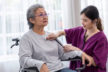 Bakıcı hemşire tekerlekli sandalyeye oturan kıdemli bir hastayla ilgilenir. Hemşire yaşlı kadına yardım ediyor.