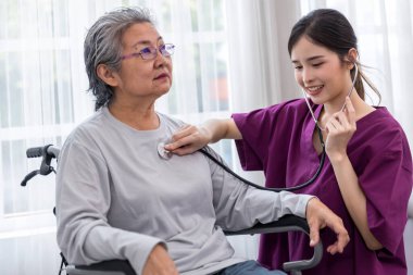 Bakıcı hemşire tekerlekli sandalyeye oturan kıdemli bir hastayla ilgilenir. Hemşire yaşlı kadına yardım ediyor.