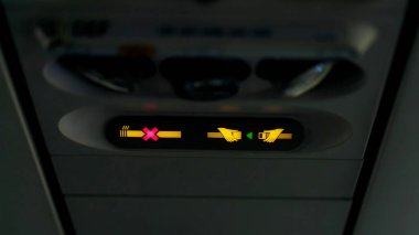 Uçaktaki yasaklama işaretleri, çapraz sigara içildiğini ve kemer takılması gerektiğini gösteren sinyaller veriyor. Lamba, emniyet kemerini bağla. Havalandırma deliğinin yanındaki uçak kalkışı için bekliyor. .