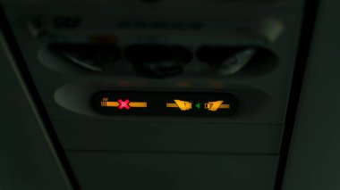 Uçaktaki yasaklama işaretleri, çapraz sigara içildiğini ve kemer takılması gerektiğini gösteren sinyaller veriyor. Lamba, emniyet kemerini bağla. Havalandırma deliğinin yanındaki uçak kalkışı için bekliyor. .