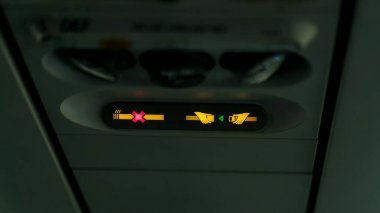 Uçaktaki yasaklama işaretleri, çapraz sigara içildiğini ve kemer takılması gerektiğini gösteren sinyaller veriyor. Lamba, emniyet kemerini bağla. Havalandırma deliğinin yanındaki uçak kalkışı için bekliyor. .