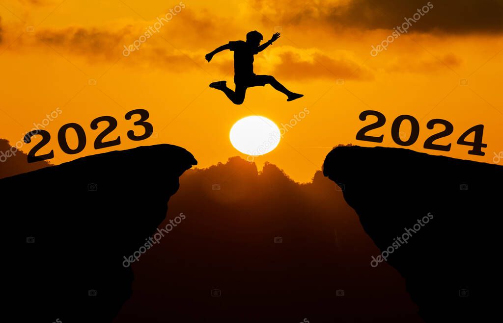 A young man jump between 2023 and 2024 years over the sun and through on the gap of hill silhouette evening colorful sky. happy new year 2023.