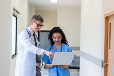 Üniformalı klinisyenler ayakta dikilip bilgisayar monitörlerine bakıyor, tıbbi belgeleri tartışıyor ve danışmanlık yapıyorlar. Doktor ve hemşire tıp bürosunda dizüstü bilgisayarla çalışıyorlar. Dizüstü bilgisayarla profesyonel tıbbi işler.