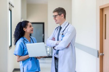 Üniformalı klinisyenler ayakta dikilip bilgisayar monitörlerine bakıyor, tıbbi belgeleri tartışıyor ve danışmanlık yapıyorlar. Doktor ve hemşire tıp bürosunda dizüstü bilgisayarla çalışıyorlar. Dizüstü bilgisayarla profesyonel tıbbi işler.