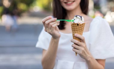 Yaz ışığı arka planında eriyen dondurmalı waffle külahını tutan eller.
