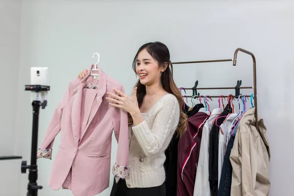 Young woman live streaming for sale fashion clothing. Woman influencer broadcast live streaming for review and sell product for online shopping brand in online social marketing.