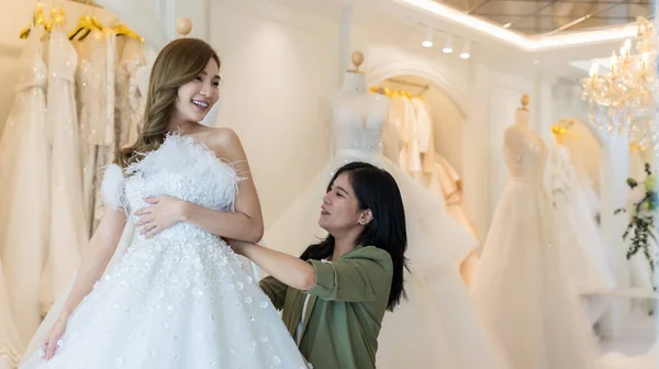 Bride wear dress and try to fitting in wedding studio with bridal store owner