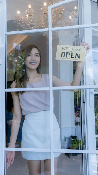 Woman store owner turning open sign broad through the door glass and ready to service. Small business woman owner turning the sign for the reopening