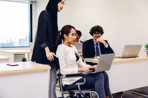 Office workers and woman on a wheelchair in bright office. They are showing a teamwork. Portrait of diverse business team with young woman in wheelchair all smiling at camera in office.