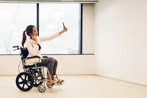 Office workers woman on a wheelchair in bright office and holding smart phone.