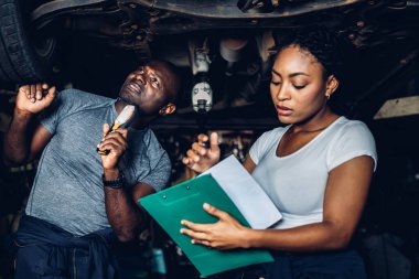 Professional Car Mechanic is Investigating Under a Vehicle on a Lift in Service. Auto Service Worker Checking Car Under Carriage Look For Issues. Car service technician check and repair customer car.