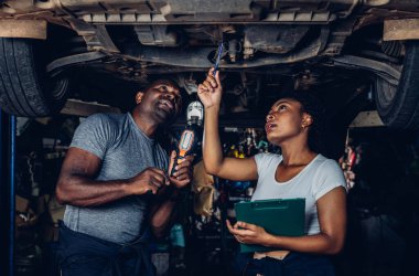 Professional Car Mechanic is Investigating Under a Vehicle on a Lift in Service. Auto Service Worker Checking Car Under Carriage Look For Issues. Car service technician check and repair customer car.