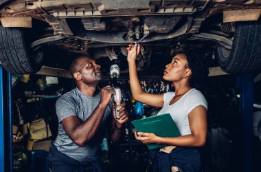 Professional Car Mechanic is Investigating Under a Vehicle on a Lift in Service. Auto Service Worker Checking Car Under Carriage Look For Issues. Car service technician check and repair customer car.