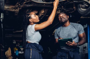 Professional Car Mechanic is Investigating Under a Vehicle on a Lift in Service. Auto Service Worker Checking Car Under Carriage Look For Issues. Car service technician check and repair customer car.