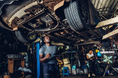 Professional Car Mechanic is Investigating Under a Vehicle on a Lift in Service. Auto Service Worker Checking Car Under Carriage Look For Issues. Car service technician check and repair customer car.