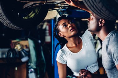 Professional Car Mechanic is Investigating Under a Vehicle on a Lift in Service. Auto Service Worker Checking Car Under Carriage Look For Issues. Car service technician check and repair customer car.