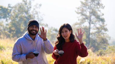Çift sabah vakti kahve içer. Genç bir çift ellerinde kupa tutarken doğanın tadını çıkarıyor..