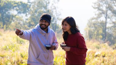 Çift sabah vakti kahve içer. Genç bir çift ellerinde kupa tutarken doğanın tadını çıkarıyor..