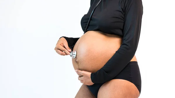 Pregnant belly. Woman standing and use stethoscope touching her naked big belly. a cute pregnant belly. belly of a pregnant woman. pregnant woman stand rest.