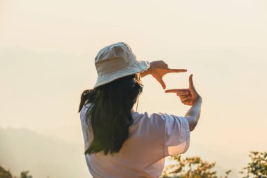 Kadın Eller, güneşin doğuşuyla uzaktan görüntüyü çerçeveliyor. Gün batımında kadın elleriyle manzara etrafında çerçeve yapıyor, gelecek planlama konsepti. İş konsepti. Yeni yıl planlama ve vizyon kavramı