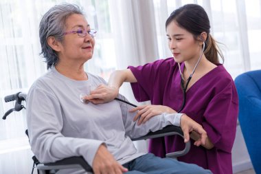 Bakıcı hemşire parkta yürüyen kıdemli bir hastayla ilgilenir. Hemşire yaşlı kadına yardım ediyor.
