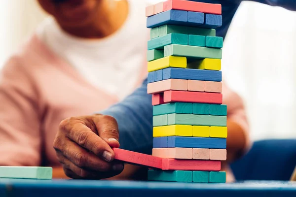 stock image Senior people playing a wooden block tower, risk and strategy of project management. Concept of business risk with domino blocks. Older People playing jenga block removal game on table at home