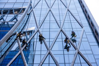 İşçiler gökdelen binasının camlarını siliyorlar. Pencere temizleyicileri modern binaların cam temizleme sınıfını temizliyorlar. Tepeden tırnağa güvenlik halatı ve temiz pencere camlarıyla süzülüyor.. 