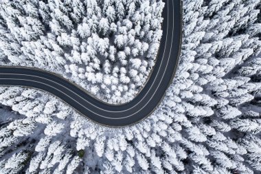 Karla kaplı ormanda yol, yukarıdan aşağıya hava manzarası. Ağaçlı ve yollu karlı dağ manzarası.