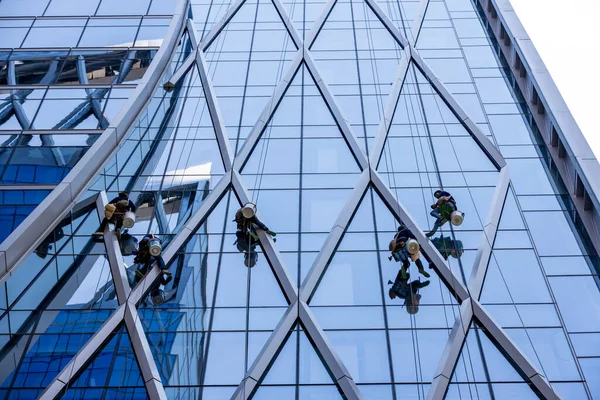 Stock image Workers washing windows of the skyscraper building. Window washer workers are cleaning window class of high modern building. Abseiling from high to low by safety rope and clean window glass by hand. 