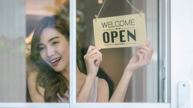 Kadın dükkan sahibinin açık tabela ile kapı camını açıp servise hazır olması. Küçük işletme sahibi kadın yeniden açılmak için tabelayı çeviriyor.