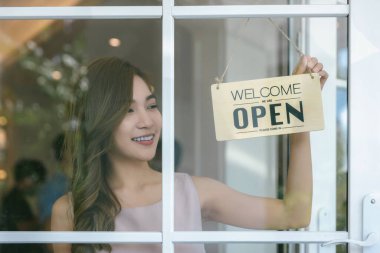 Kadın dükkan sahibinin açık tabela ile kapı camını açıp servise hazır olması. Küçük işletme sahibi kadın yeniden açılmak için tabelayı çeviriyor.