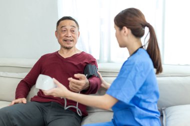 Bakıcı hemşire kan basıncını ölçmek için evdeki yaşlı hastayı kullanıyor. Bakıcı hemşire kan basıncını ölçmek için tıbbi cihaz kullanıyor..