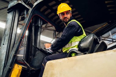 Forklift sürücüsünde çalışan adam fabrika lojistik gemisinde çalışmaktan mutlu. Depoda forklift şoförü var. Forklift sürücüsü depoda araçta oturuyor.