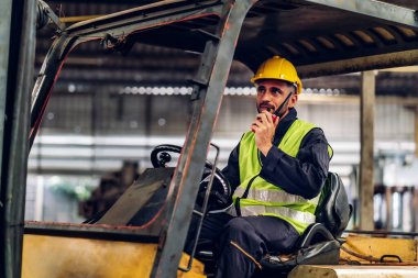 Forklift sürücüsünde çalışan adam fabrika lojistik gemisinde çalışmaktan mutlu. Depoda forklift şoförü var. Forklift sürücüsü depoda araçta oturuyor.