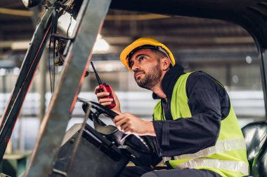 Forklift sürücüsünde çalışan adam fabrika lojistik gemisinde çalışmaktan mutlu. Depoda forklift şoförü var. Forklift sürücüsü depoda araçta oturuyor.