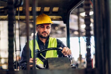 Forklift sürücüsünde çalışan adam fabrika lojistik gemisinde çalışmaktan mutlu. Depoda forklift şoförü var. Forklift sürücüsü depoda araçta oturuyor.